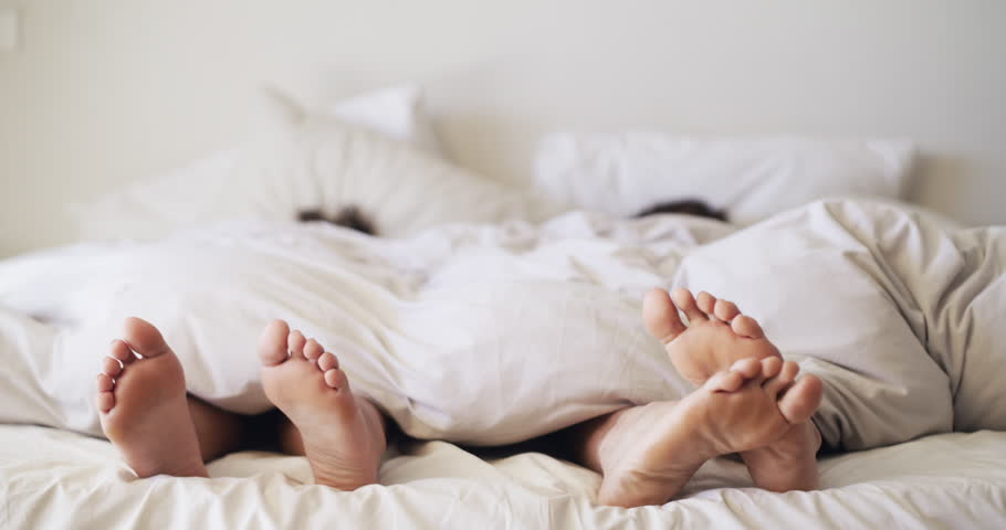 Love, sleep and feet with a couple in bed to relax together in their home on a weekend morning. Happy, peace or romance with a man and woman in the bedroom of their apartment for bonding or affection