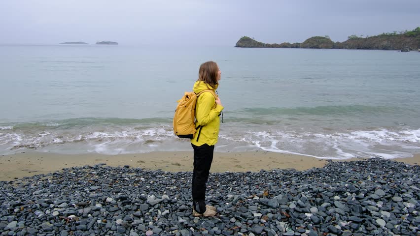 Young woman walks alone along cold Turkish coast. Windy, cloudy weather, peaceful solitude and gentle connection with nature by stormy sea.