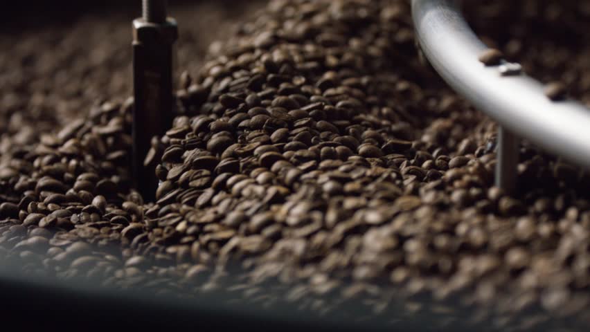 Professional coffee roasting equipment mixing freshly roasted coffee beans, revealing dark brown texture and rich roasting process inside industrial metal machine