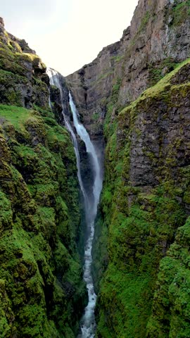 Witness the majestic waterfall flowing down rocky cliffs, surrounded by vibrant greenery in a remote Icelandic canyon. Glymur waterfall canyon in Iceland