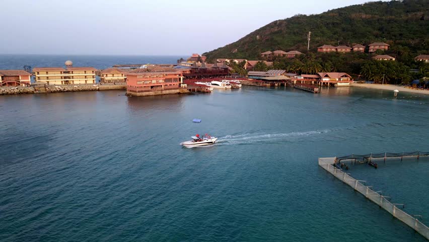 Experience the stunning aerial perspective of Sanya as the sun sets behind the horizon. The warm colors illuminate the marina and coastline, creating a tranquil atmosphere.