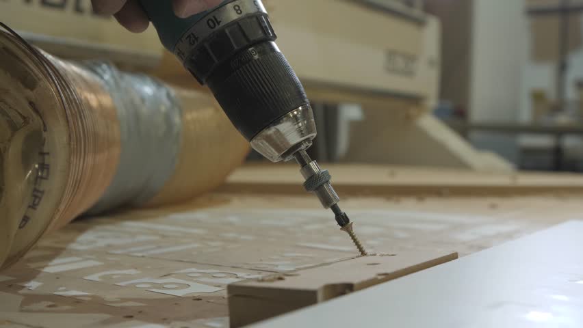 Furniture manufacturing process showcasing a carpenter tightening screws with a power drill and positioning a wooden piece on a workbench