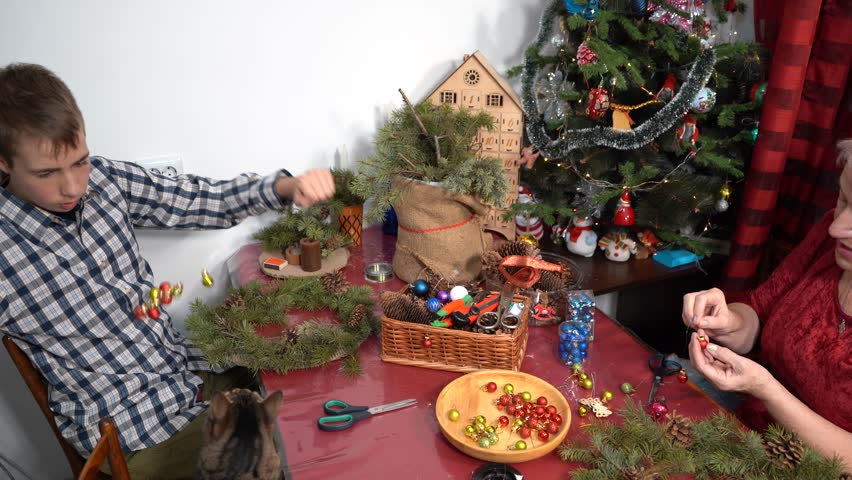 Boy playing with cat. Grandmother makes Christmas wreath. Elderly woman and teenager spend time together in winter. Family fun.