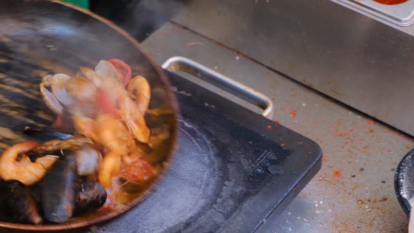 A chef quickly shakes a pan while stir-frying seafood from the Asian coast. Shellfish, oysters, and shrimp sizzle in the pan with spices. A vibrant dish from Mediterranean or Central Asian cuisine.