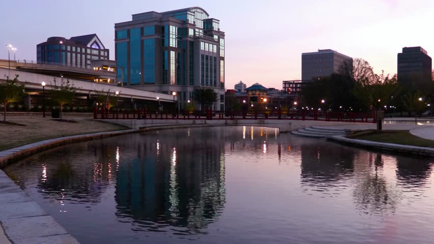 City buildings reflect in a pond at dusk