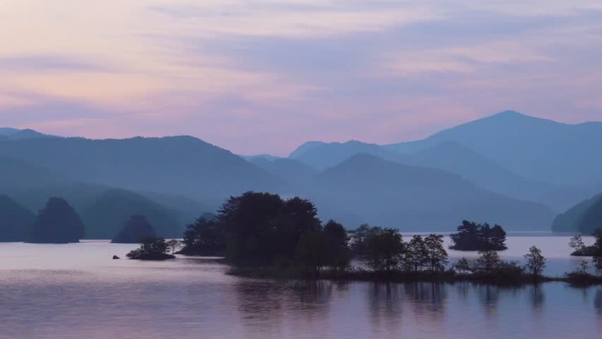 Mountains and islands reflect in a tranquil lake at dusk