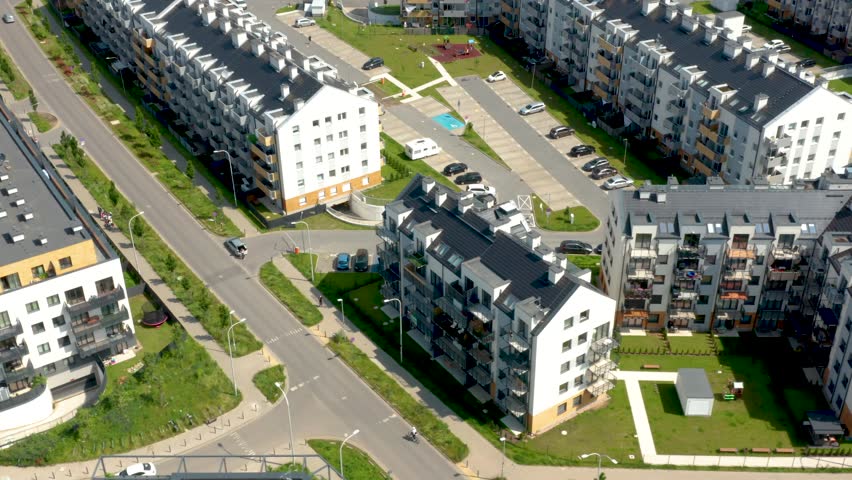 This oblique aerial sequence surveys suburban apartment buildings with manicured lawns and balconies, showcasing summer light to highlight architectural design for real estate promotion.