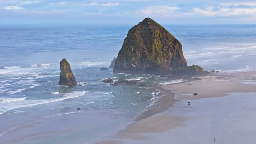 High aerial telephoto shot of stunning Haystack Rock, with sunlight cast onto the foggy beach, creating a moody coastal morning scene at Cannon Beach, Oregon