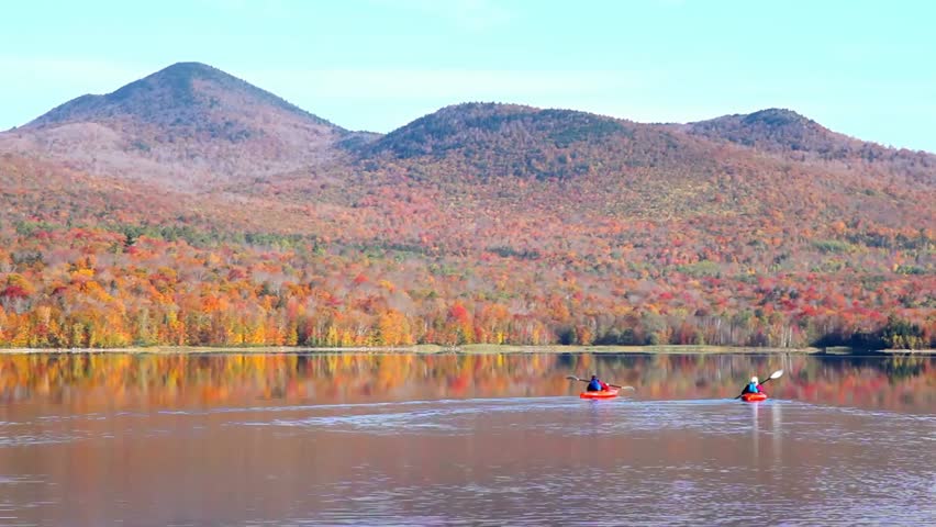 Kayakers paddle on a lake surrounded by autumn mountains