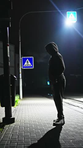 A Ghostly figure elegantly stretches and exercises under a street lamp in the darkness of the night. Intriguing Nighttime Urban Scene, filled with action and energy. Vertical video