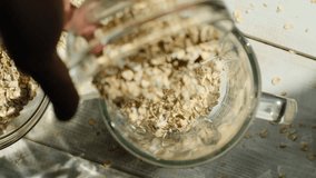 Top view shot of a hand pouring whole dry oat flakes from a container into a blender to grind into flour for fiber rich vegetarian bread, a low calorie alternative to wheat. - Powered by Shutterstock - Get 15% off with code: PIKWIZARD15