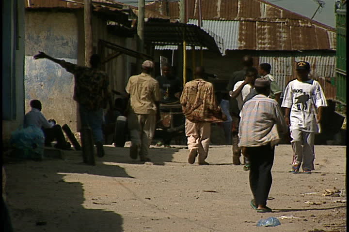 DAR ES SALAAM, TANZANIA - DECEMBER 1, 1998: Young men and boys walking on dirt road between buildings.