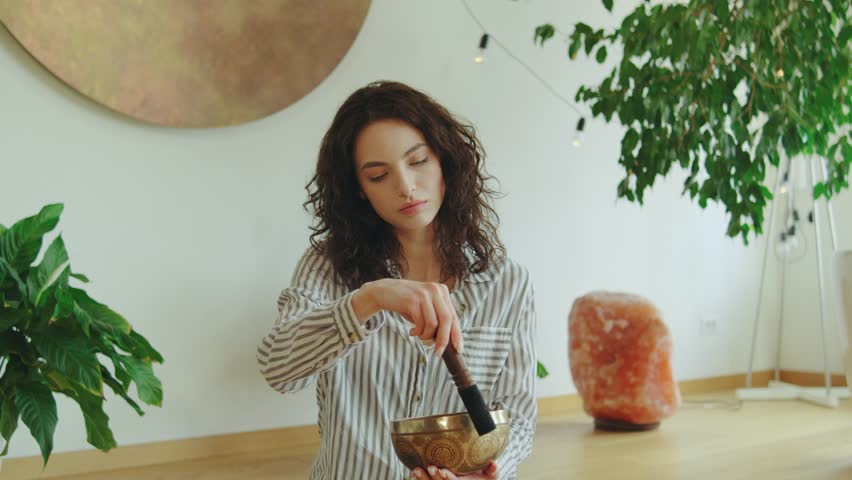 Meditation session in a serene indoor space with a young woman using a singing bowl for relaxation and mindfulness practice