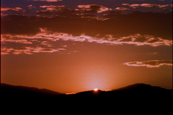LOS ALAMOS, NEW MEXICO - CIRCA SEPTEMBER 1998: Fireball sun rises behind the Jemez mountains under an orange sky and illuminated clouds