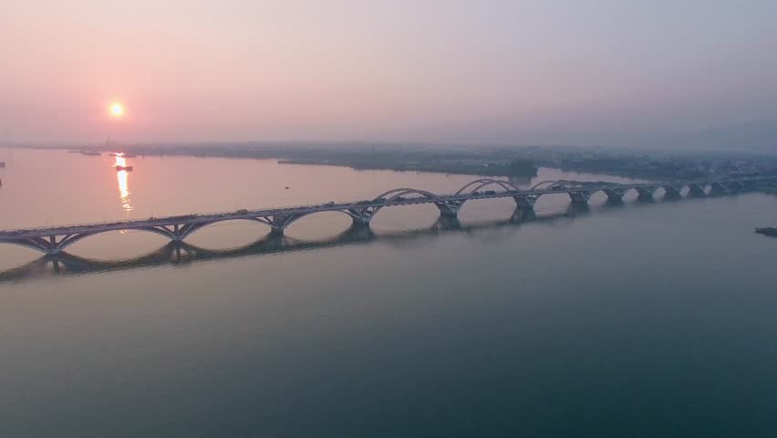Witness the elegant Qingyuan Bridge from above as the sun rises, casting warm colors over the tranquil water. The bridge showcases unique architectural design amidst a serene landscape.
