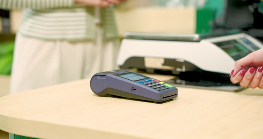 Asian female customer tapping credit card on contactless terminal to pay for purchase at modern small fruit shop highlighting electronic transaction in clean indoor environment