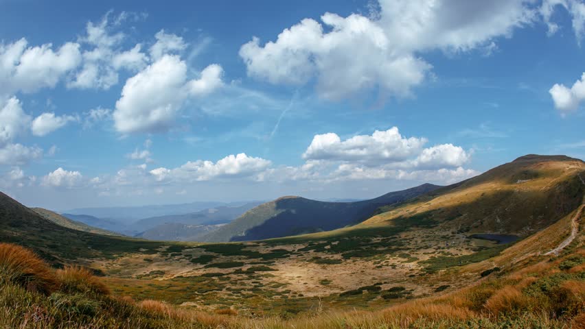 Time-lapse of scenic Carpathian Mountains near Hoverla showing clouds drifting across blue sky over a golden valley. High quality nature footage perfect for promos, ads, or travel edits.