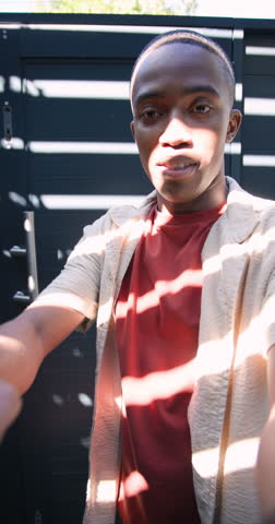 Vertical video: Sunlight urging African American man with camera opening gate entering yard to vlog. Vlog, lifestyle, outdoor, greenery, casual, nature, vertical video