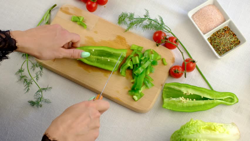 Chopping green peppers and fresh cherry tomatoes on wooden cutting board