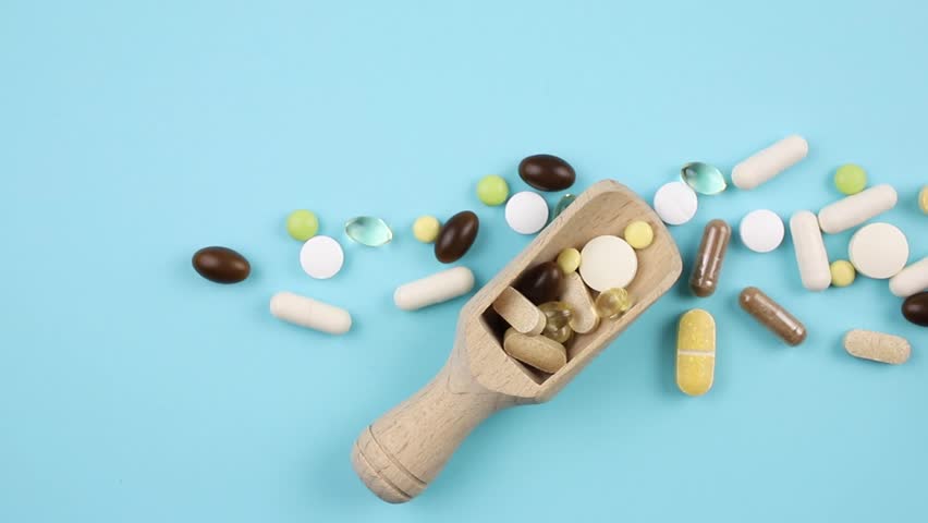 Two vintage natural wood spoons filled with various pills and capsules. Selective focus, light blue color background.