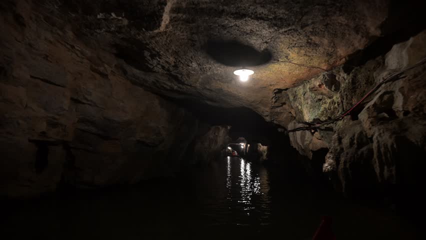 Boat navigating underground river through Trang An Grotto, revealing geological wonders and hidden natural landscape in dark subterranean environment