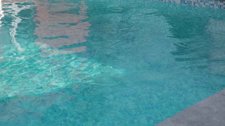 Blue water in a swimming pool with building reflections and visible mosaic tiles at the bottom. Gentle ripples create a dynamic play of light and color
