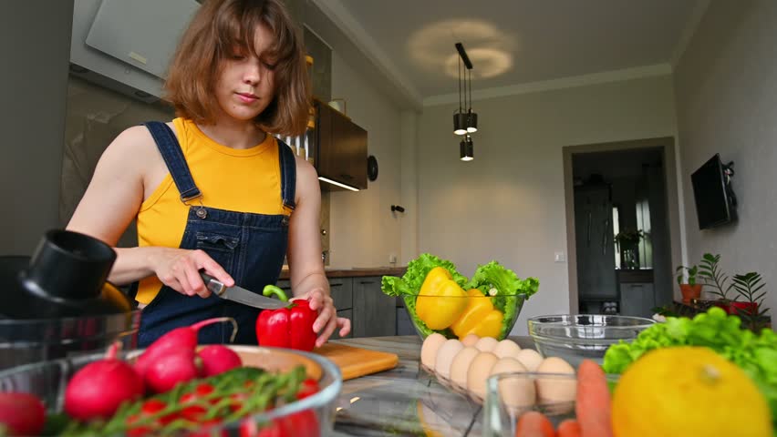 woman in the kitchen inspects and evaluates the freshness of peppers before cutting them into a salad. A girl with healthy vegetables prepares a snack while relaxing at home