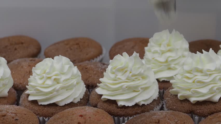 Pastry chef skillfully decorating cupcakes with smooth white cream from a piping bag, creating an exquisite dessert in a bustling professional kitchen filled with delicious aromas slow motion