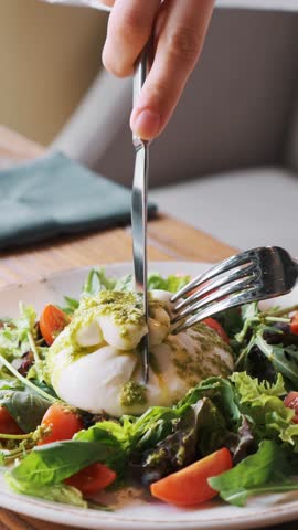 Salad with arugula, cherry tomatoes, and burrata with pesto sauce on a white plate in a cafe. A woman