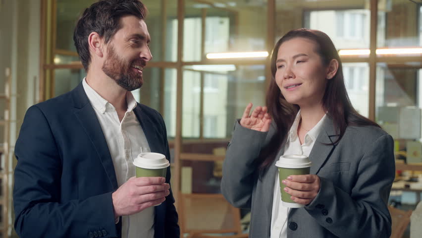 Happy laughing business coworkers drinking coffee break friendly talking at office Caucasian Korean businessman businesswoman work resting employees share ideas conversation woman man paper cup drink