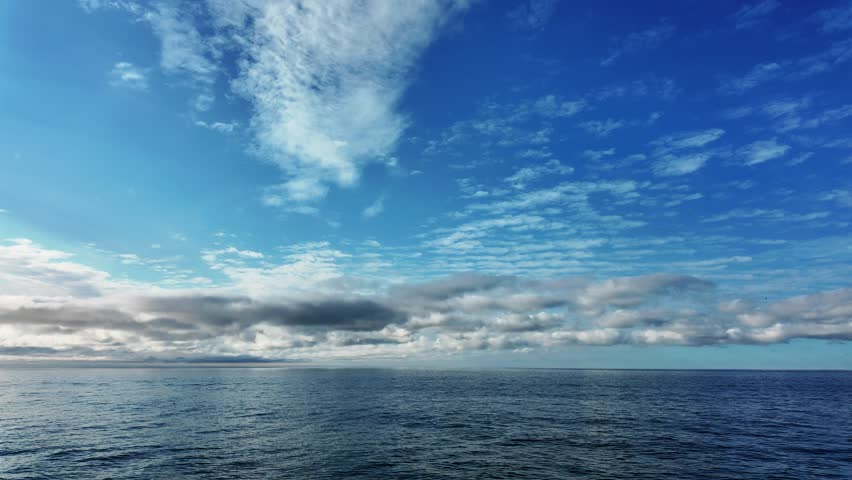 Peaceful seascape with smooth water and expansive sky covered in white clouds.