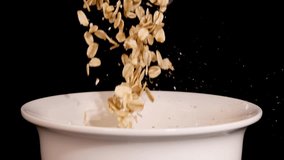 Oat grains cascade into a white bowl against a black backdrop, creating a dynamic and textured visual - Powered by Shutterstock - Get 15% off with code: PIKWIZARD15