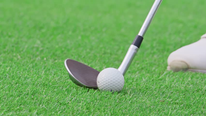 Close up of professional golfer swinging club on a scenic golf course. The shot captures the precise moment of striking the golf ball on the well maintained green fairway.