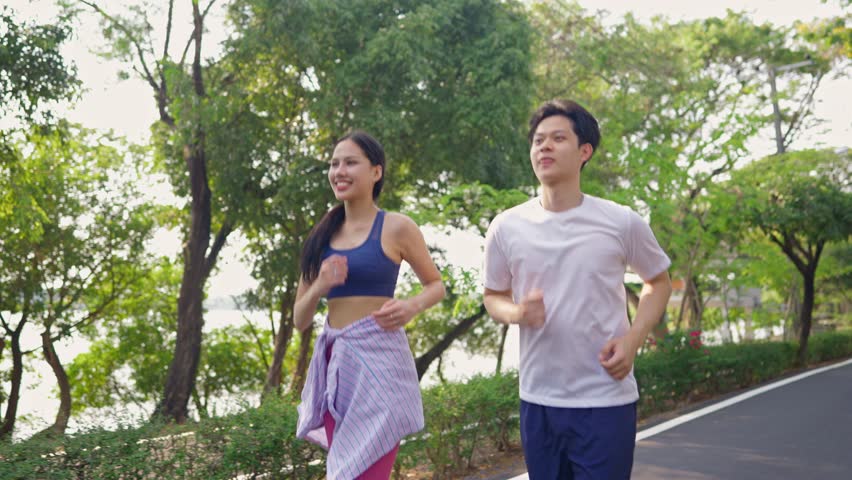 Asian young couple doing running exercise in the morning outdoors garden. Attractive man and woman feel happy and relax, spend their romantic day jogging side by side through a beautiful garden path.