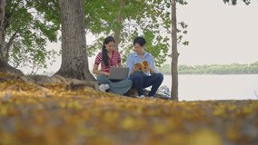 Asian young couple spend time on a romantic date in the outdoors garden. Attractive man and woman feel happy and relax, with one using laptop and the other reading a book while having picnic in park. - Powered by Shutterstock - Get 15% off with code: PIKWIZARD15