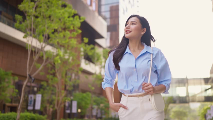 Asian young beautiful businesswoman walking outdoors in modern city. Attractive employee girl worker feel happy and confident walking around outside building, going to the office in early morning.
