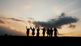 Silhouettes of a group of people, men and women, enjoying a country holiday. A group of seven people walk out into the sunset, holding hands and raising them up. - Powered by Shutterstock - Get 15% off with code: PIKWIZARD15