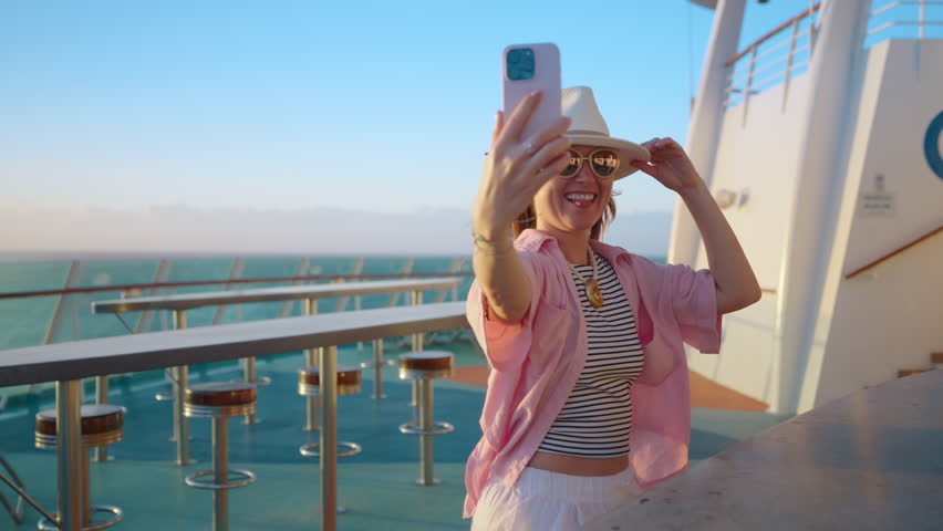 A joyful woman enjoys a beautiful sunset cruise, capturing playful selfies against the stunning ocean backdrop. These moments at sea are perfect for fun, relaxation, and creating lasting memories