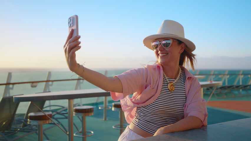 A joyful woman enjoys a beautiful sunset cruise, capturing playful selfies against the stunning ocean backdrop. These moments at sea are perfect for fun, relaxation, and creating lasting memories
