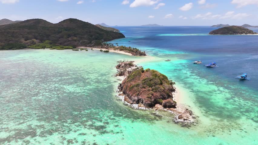 Aerial view of Bulog Dos Island in the Philippines with vivid turquoise waters, a connecting sandbar, coral reefs, forested islets, and anchored boats under bright tropical skies