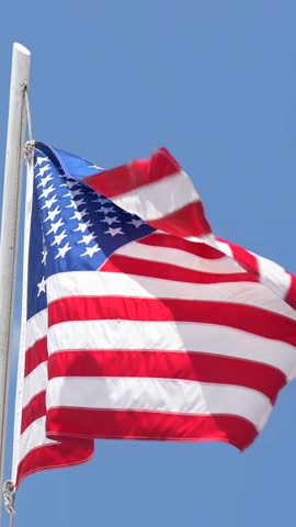 Vertical shot of full National American flag waving on a pole against clear blue sky