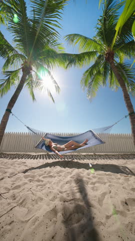 Vertical Screen: A serene beach shows a person relaxing in a hammock between palm trees, basking in warm sunlight under a clear blue sky, perfect for unwinding and enjoying nature