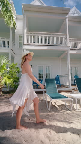 Vertical Screen: On a serene beach day in sunny Key West, a woman strolls along the sandy shore, enjoying the breathtaking view near a picturesque beach house, the perfect coastal retreat