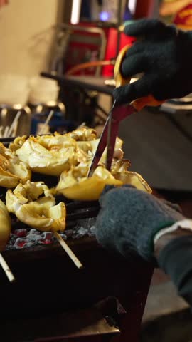 Vertical Close-up of grilled seafood skewers on stick. Man hand cutting with scissors and flip. Yaowarat Road in Chinatown - popular night market for try street food. Bangkok, Thailand