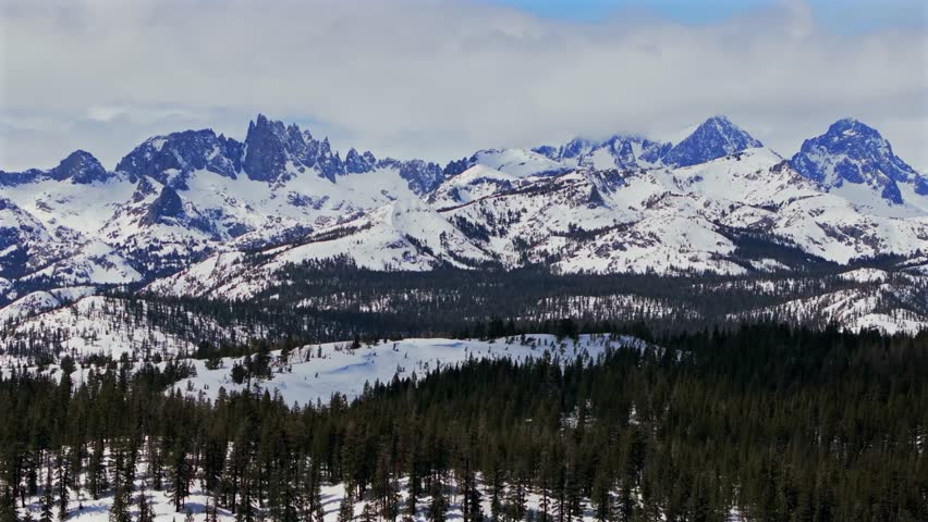 Banner peak Volcanic ridge Minaret Summit Pass Mammoth Mountains vista Parallax winter aerial drone California group jagged towering snow covered peaks sunny blue sky Inyo forest Sierras PCT upwards
