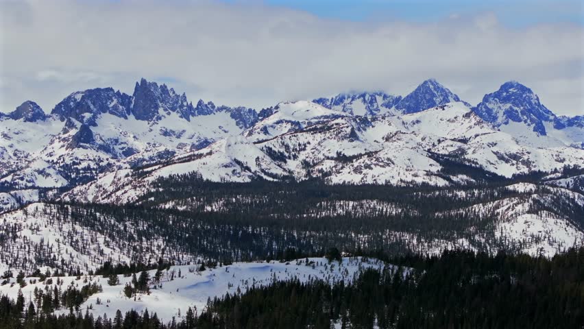 Banner peak Minaret Summit Pass Mammoth Mountains vista Parallax winter aerial drone California group jagged towering snow covered peaks sunny blue sky Inyo forest Sierra Nevada valley backwards