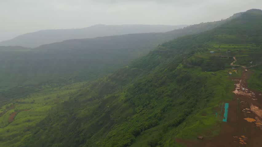 A drone captures lush green mountains of Panchgani, Maharashtra, draped in monsoon mist. Rolling hills vanish into the fog, creating a serene and mystical landscape 4K