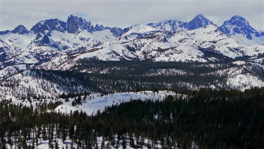 Banner peak Minaret Summit Pass Mammoth Mountains vista Parallax winter aerial drone California group jagged towering snow covered peaks sunny storm Inyo forest Sierra Nevada valley forward pan up