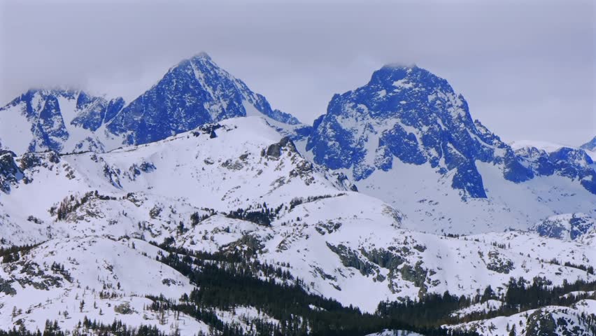 Banner peak Minaret Summit Pass Mammoth Mountains vista Parallax winter aerial drone California group jagged towering snow covered peaks wind fog cloudy daytime alpine Sierra Nevada valley pan left