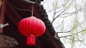 A red Chinese lantern sways gently under a tiled roof, framed by tree branches. Ideal for cultural, seasonal, festive, or travel-themed visual projects. - Powered by Shutterstock - Get 15% off with code: PIKWIZARD15